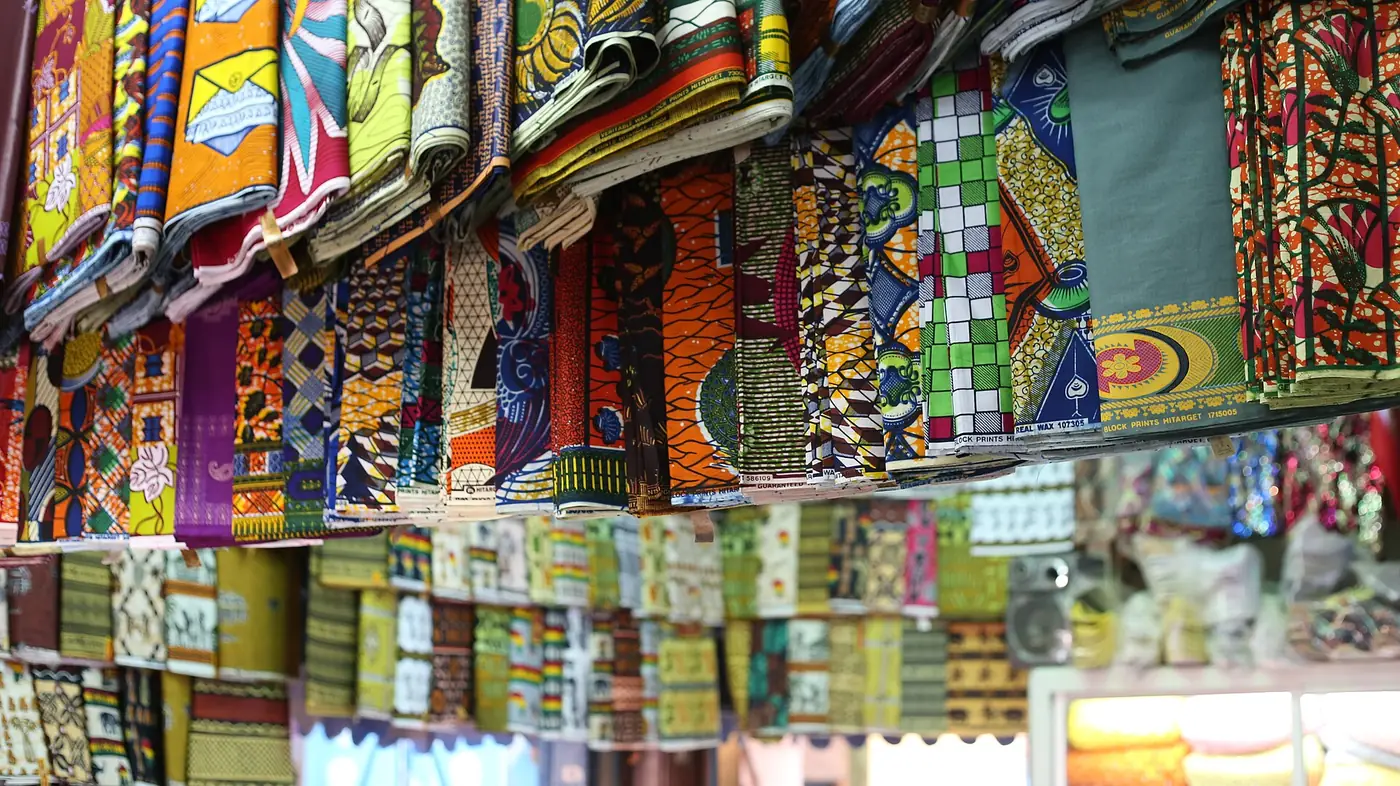 Des rouleaux de tissus wax aux motifs colorés empilés sur des étagères.